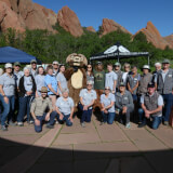 25 volunteers and staff with mascots pose at an event at the park
