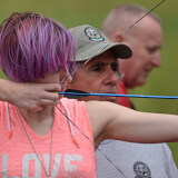 Young person practices archery with volunteer support