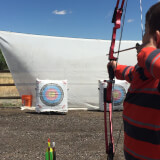 An older child has a bow pulled back and is aiming at a target. 